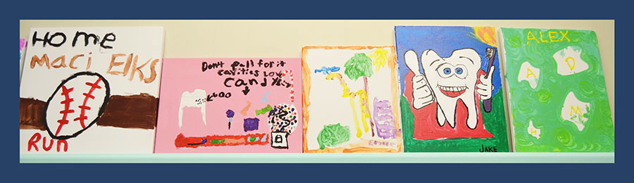 The image shows a collection of colorful drawings or paintings with various subjects displayed on a wall, possibly part of an exhibition or gallery setting.