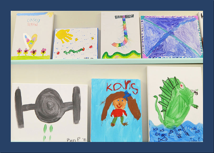 The image displays a collection of colorful children's artwork displayed on a table or shelf.