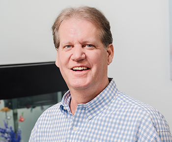 The image features a man with a smile, standing behind a large, blue bubble-like structure.