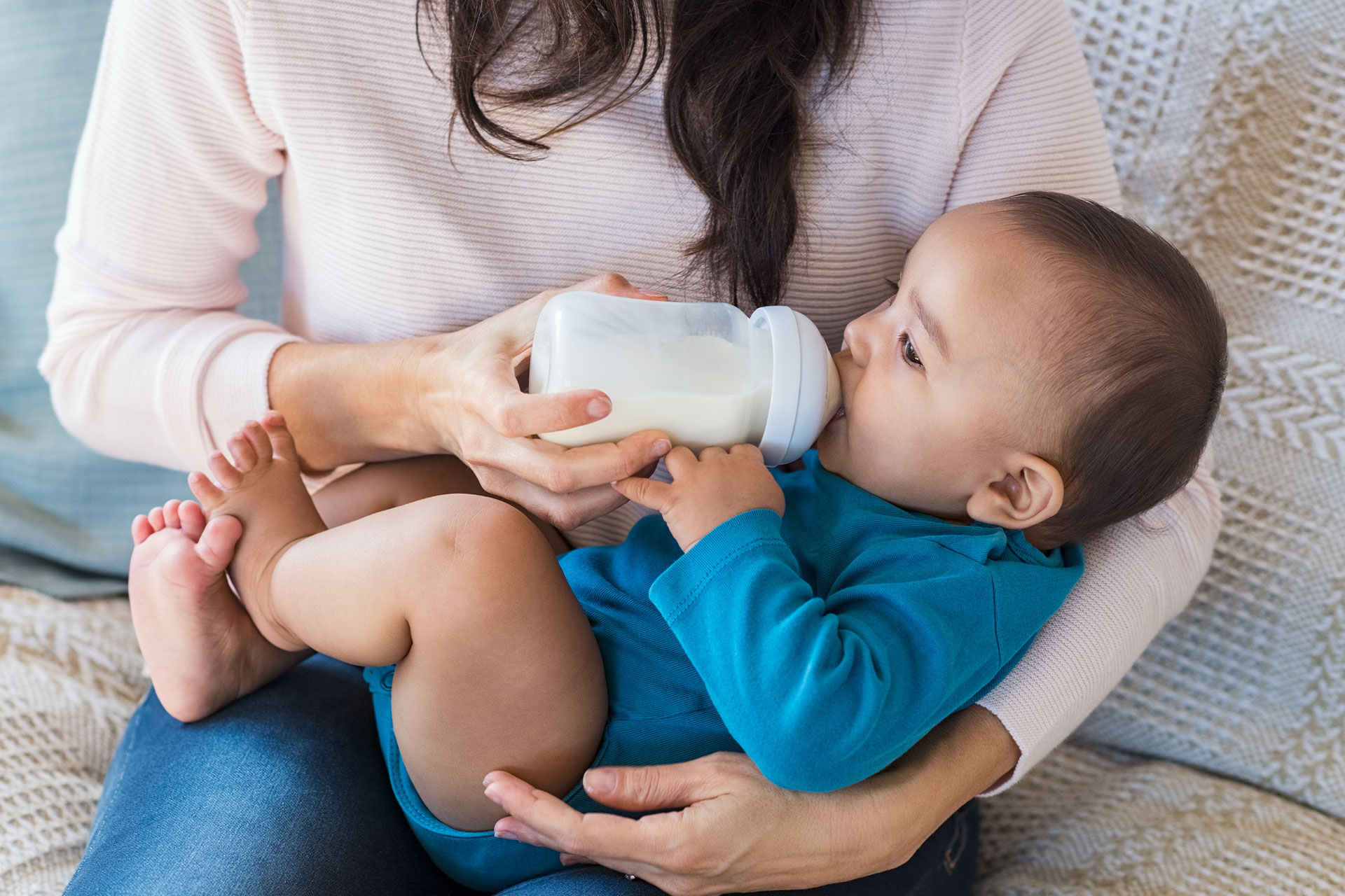 A woman feeding a baby with a bottle while seated on a couch.