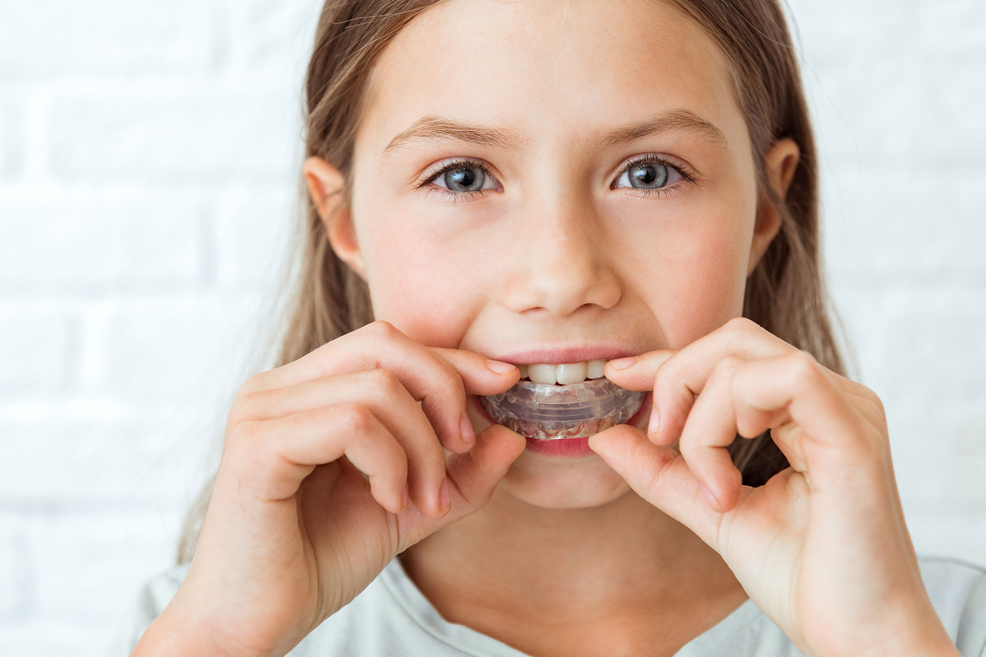 A young girl with braces holding a toothbrush in her mouth.